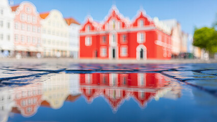 Obraz premium Vibrant red historic building reflected in a wet cobblestone street after rain