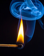 Burning match with bright flame and blue smoke on dark backdrop.