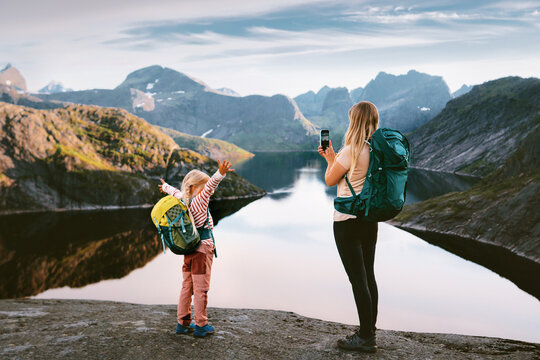 Family travel in Norway mother hiking with child taking photo using smartphone mountains and lake view explore Lofoten islands together, active summer vacations backpacking trip outdoor