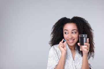 Beautiful Brazilian woman with glass of water and collagen pill on gray background. Space for text