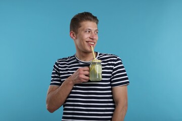 Smiling man drinking lemonade from mason jar on light blue background. Refreshing drink