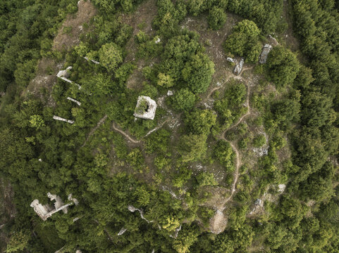 Aerial view of ancient ruins nestled amidst dense green foliage, a stark contrast between stone and nature's embrace in Frattura Vecchia, Scanno, Abruzzo, Italy.