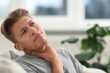Young man suffering from sore throat at home. Space for text