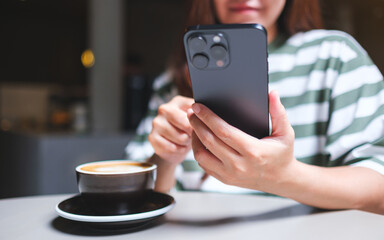 Closeup image of a woman holding and using mobile phone in cafe