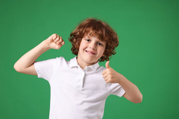Strength. Happy little boy showing his biceps and thumbs up on green background