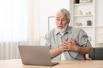 Senior man having online consultation with doctor via laptop at table indoors
