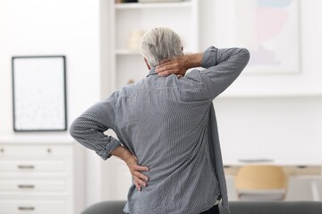 Senior man suffering from neck pain at home, back view