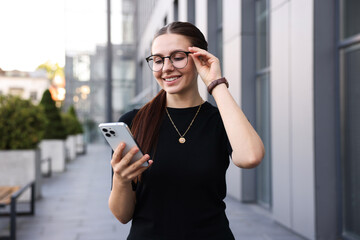 Successful businesswoman with smartphone near office building