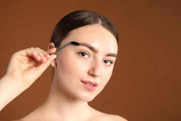 Fototapeta premium Young woman brushing her eyebrow with spoolie on brown background