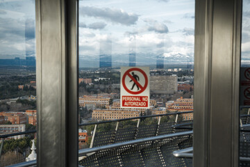 Panoramic city view from high-rise building with warning sign in foreground during overcast...
