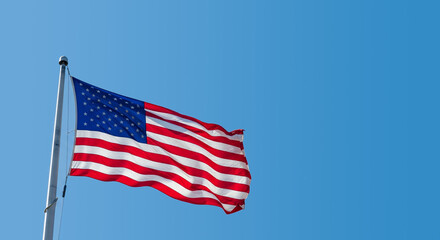 Fototapeta premium The American flag waving proudly in the wind against a clear blue sky