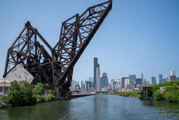 Historic drawbridge towers over the skyline of downtown Chicago on a clear sunny day with a river flowing beneath