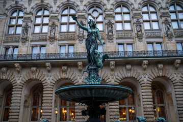 Majestic fountain featuring a woman holding a bowl, set in front of ornate building architecture in an urban plaza during early evening hours