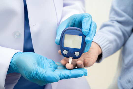 Asian doctor using digital glucose meter for check sample blood sugar level to treatment diabetes.
