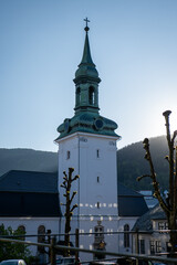 Historic church with a spire standing beneath a clear blue sky at sunset in a scenic mountain...