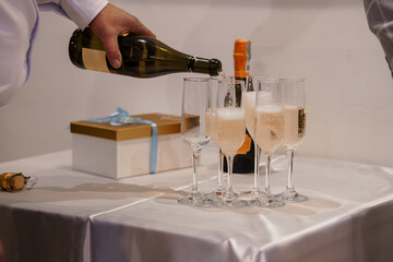 Champagne Pouring Celebration with Bubbles, Gift Box, and Festive Glasses on White Tablecloth, Soft...