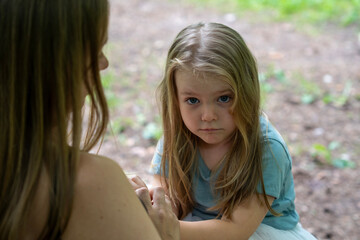 Naughty child sitting on mother's lap and looking over mothers's shoulder. A candid emotional...