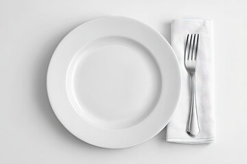 Overhead view of a minimalist place setting a large white dinner plate beside a fork nestled in a small white napkin on a white background