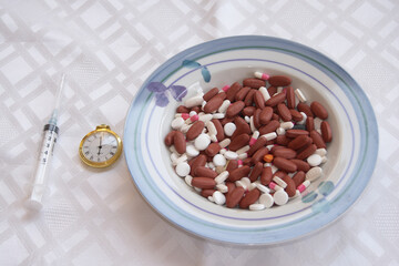 bowl of pills, a golden pocket watch, and syringe on white. representing health, time, and medical treatment