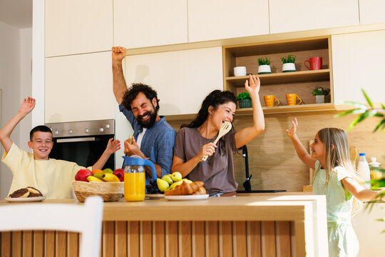 Happy family singing and dancing in kitchen while having breakfast