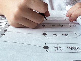 A young student sits at a wooden desk working on basic math exercises, steadily developing essential problem solving skills.