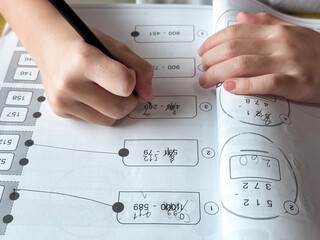 A young student sits at a wooden desk working on basic math exercises, steadily developing essential problem solving skills.
