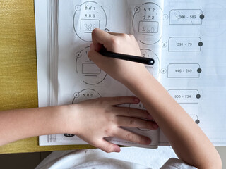 A young student sits at a wooden desk working on basic math exercises, steadily developing essential problem solving skills.