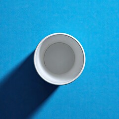 Overhead view of an empty, white paper cup on a vibrant blue background, casting a subtle shadow