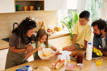 Smiling family preparing breakfast together in a modern kitchen, whisking eggs and enjoying quality...