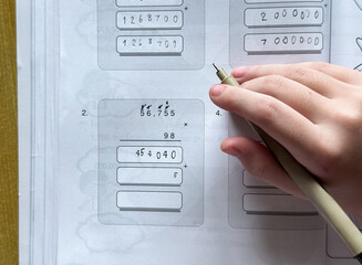 A young student sits at a wooden desk working on basic math exercises, steadily developing essential problem solving skills.