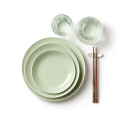 Pale green ceramic plates, nested, with two glasses of water and chopsticks on a white background, viewed from above