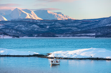 Fisher shelter in winter with fishboat at sunset in the background snowy mountains and Norwegian fjords - Tromso, Norway
