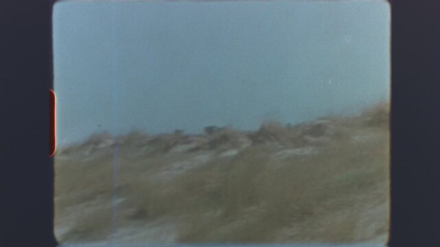Coastal dunes and sea view with a person walking along the beach on retro super 8mm vintage film