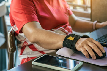 Hands of woman with thumb spica finger splint using computer mouse  to work. Woman work on desk...