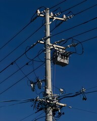 A utility pole with tangled electrical wires against a clear blue sky.