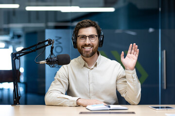 Portrait of a young smiling man in headphones sitting in the office at a desk in front of a...