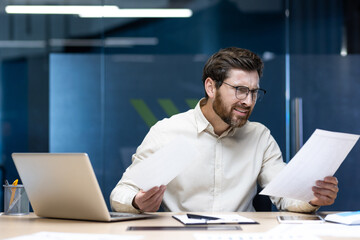 An angry young man sits at his desk in the office and reads the received letter and documents