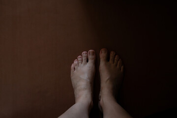 Female bare feet standing on brown floor in semi-darkness in apartment