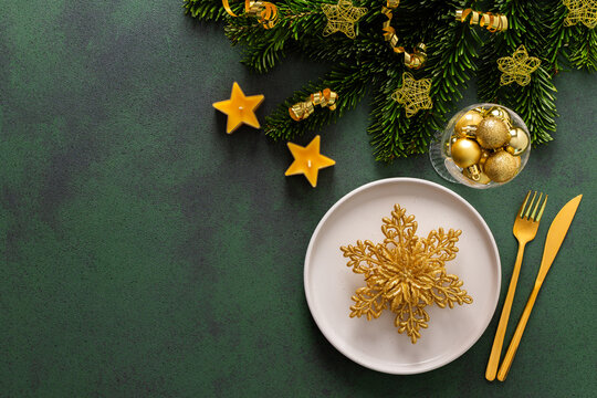 Top view of a Christmas table, featuring an empty plate with cutlery on a green surface. Spruse branches and golden tree decorations set a joyful holiday atmosphere
