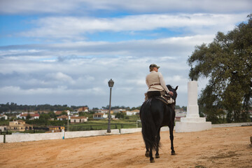 Young female horsewoman riding a black Spanish thoroughbred horse, trotting with him, seen from the...