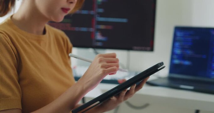 Closeup young Asia female freelance write code on tablet while work prompt AI IT app smart program nomad, video game, terminal coding, user interface, data center on desktop computer at home office.