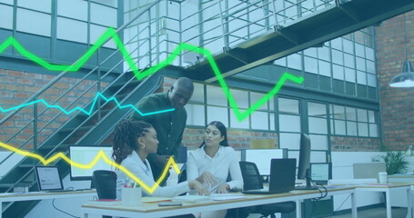 Analyzing colleagues reviewing financial data on monitors in loft office, with graph overlays