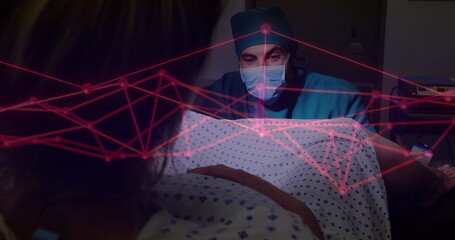 Examining doctor leaning over patient in patterned gown on hospital bed, with red digital overlay
