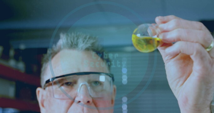 Senior scientist wearing lab coat and safety glasses, examining round flask of yellow liquid in lab - Powered by Adobe