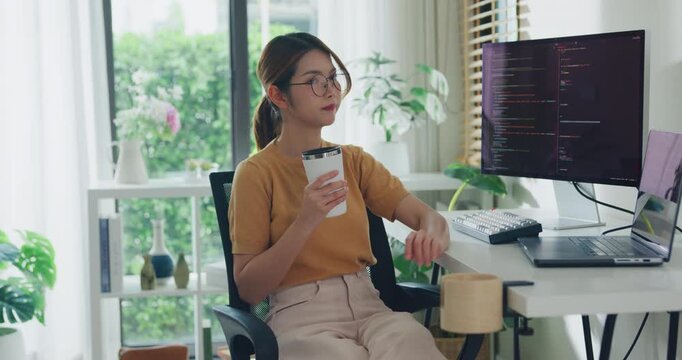 Young Asia female freelance eyeglasses drink coffee and type write prompt AI bot IT app program nomad, video game, terminal with coding, user interface, data center on desktop computer at home office.