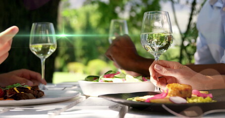 Trio holding wine glasses at white garden table with salads, grilled meat, corncake, pickles