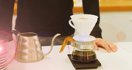 Dark sweater barista pouring pour-over coffee at kitchen counter, with dripper and gooseneck kettle