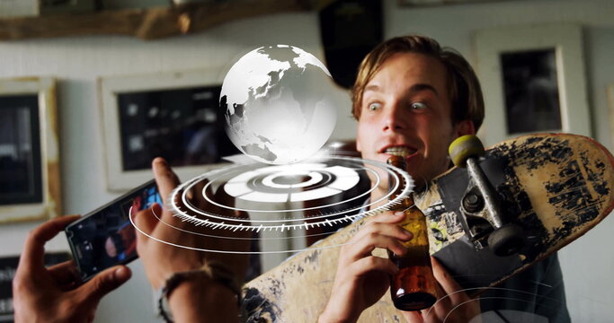 Holding phone filming friend in tee holding skateboard and bottle, AR globe overlaying in studio