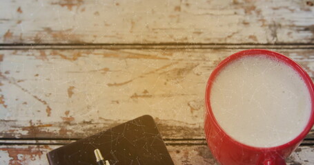 Resting red ceramic mug with frothy coffee on cafe wooden tabletop, with notebook, pen, copy space
