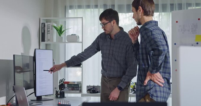 Team adult male engineer collaborate on robotic hand project using AI code solutions machine learning at tech workspace. Artificial intelligence interface, collaboration support prototype development.